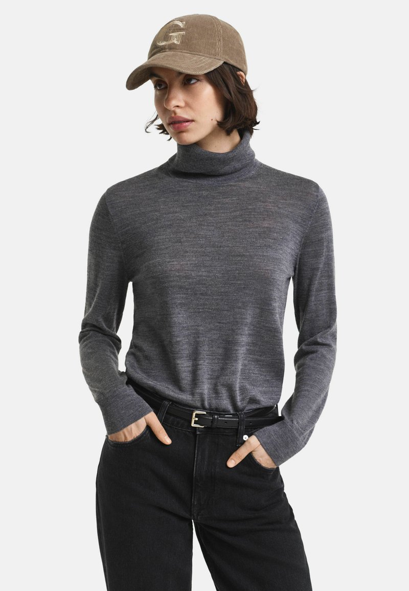 Grijze turtleneck trui met lange mouwen, gemaakt van een zachte stof. Gecombineerd met zwarte jeans en een beige corduroy pet met een logo.