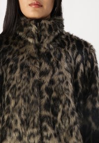 Giacca in pelliccia artificiale nera e marrone con colletto alto, caratterizzata da una stampa leopardata e chiusura con zip frontale. Tessuto morbido e texturizzato.