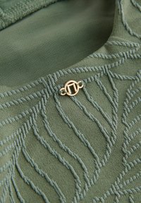 Material texturat verde, cu linii ondulate ridicate și un accent circular auriu. Modelul adaugă profunzime și dimensiune materialului.