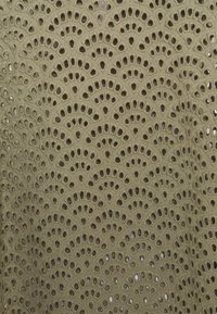 Grüner bestickter Stoff mit einem sich wiederholenden Fächerdesign und kreisförmigen Ausschnitten, die ein strukturiertes, geschichtetes Erscheinungsbild erzeugen.