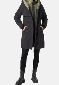 Svart parka med huva, kontrasterande olivegrön foder, knapplås och dragkedja, två framfickor och strukturerad väv.