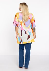 Tunique multicolore présentant un mélange de formes abstraites en violet, rose, jaune et orange. Tissu doux avec des manches courtes et larges et une coupe ample.