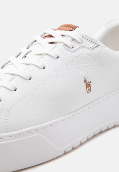 Άσπρο δερμάτινο αθλητικό παπούτσι με άσπρες κορδόνια, καφέ δερμάτινο ταμπελάκι στη γλώσσα και μικρό κεντημένο λογότυπο παίκτη πόλο στη πλευρά.