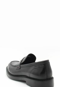 Mocassin en cuir noir avec une finition lisse, un bout arrondi et un talon bas. Présente des coutures décoratives et un branding subtil sur le côté.