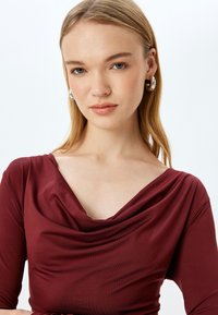 Bordeaux cowl-neck top met driekwartmouwen, gemaakt van soepele, rekbare stof, met subtiele plooidetails bij de halslijn.