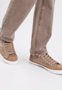 Zapatillas altas de lona beige con suelas de goma blanca, cordones planos y detalles de costura. Combinadas con pantalones tapered beige.