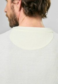 Svetr z waffle pleteniny v barvě off-white s kulatým výstřihem a texturovaným vzorem. Obsahuje hladký, kontrastní zaoblený detail na zádové partii.