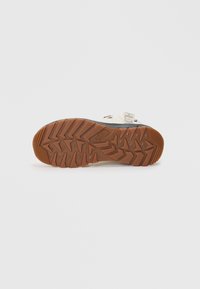 Sole of a shoe featuring a brown rubber material with a textured zigzag pattern, accented by a black section at the edge and brand logo.