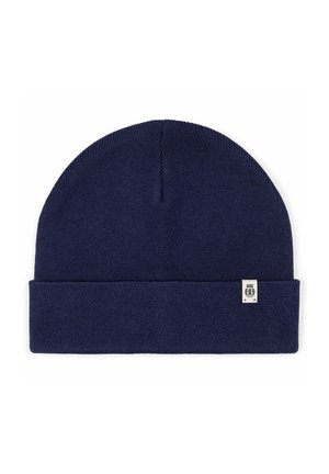 Navy blue knit beanie with folded cuff and small white rectangular tag featuring a black emblem on the cuff's lower edge.