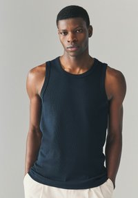 Schwarzes geripptes Tanktop mit rundem Ausschnitt und ärmellosem Design, das eine figurbetonte Silhouette und eine glatte Textur aufweist.