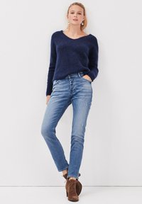 Suéter de lana azul marino con cuello en V, combinado con jeans de mezclilla desgastados de color azul claro y botas de ante marrón hasta el tobillo con cordones.