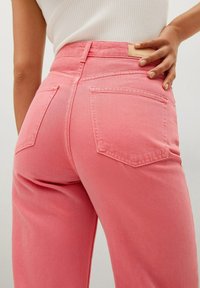 Pantalon en jean rose taille haute, avec deux poches arrière et des détails de couture. Texture lisse et coupe ajustée, illustrant un design décontracté.