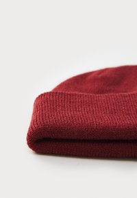 Rød strikket lue med oppbrett, med et strukturert, ribbestrikket mønster og mykt stoff.