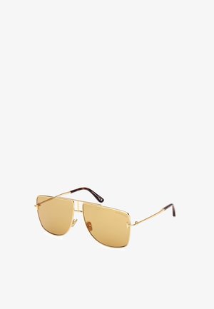 Zlaté sluneční brýle s jantarovými skly, ostrý tvar, tenké nožičky a hnědé acetátové konce. Vyznačují se minimalistickým designem a vyrytým logem.