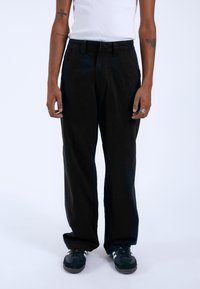 Pantalones de pierna ancha negros, hechos de tela texturizada, con una cinturilla alta y bolsillos frontales, combinados con una blusa sin mangas blanca y zapatillas negras.