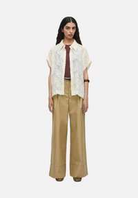 Camisa de botones de encaje en color off-white sobre una camiseta burdeos, combinada con pantalones anchos de color caqui y zapatos de plataforma marrones. Textura suave.
