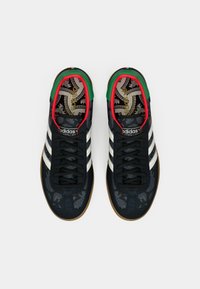 Čierne semišové tenisky s tromi bielymi pruhmi, vzorovanou stielkou, zelenými a červenými prvkami na golieri a podrážkou z gumy.
