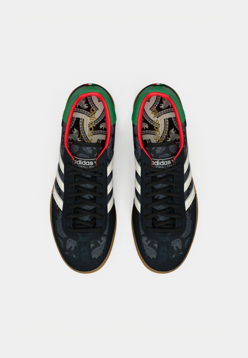 Sorte ruskinds-sneakers med tre hvide striber, mønstret indersål, grønne og røde accenter på støvlekanten og sål i gummegummi.