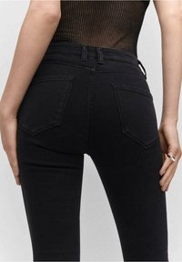 Vaqueros negros de talle alto con ajuste slim, diseño de cinco bolsillos y un sutil detalle de costura en los bolsillos traseros. Textura de denim suave.