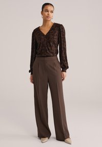 Temno rjava bluza z rožnatim vzorcem in gumbi, združena z visokim pasom, širokimi rjavimi hlačami in ostrimi bež čevlji.