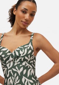 Bañador verde con un patrón de hojas en blanco. Presenta tirantes ajustables, un diseño cruzado en el busto y una textura suave.