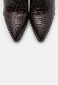 Botas de tobillo de punta afilada y color marrón, hechas de cuero brillante con estampado de cocodrilo, con una textura suave y un tacón delgado y minimalista.