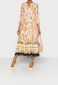 Kukallinen, pitkähihainen mekko V-aukolla, jossa on eloisat värit ja kuosit. Yhdistetty keltaisiin korkokenkiin ja vaaleanpunaiseen käsilaukkuun.