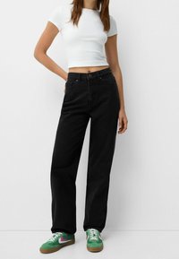 Jeans negros de talle alto con un corte relajado, combinados con una camiseta blanca corta. Acuñados por zapatillas verdes con rayas rosas.