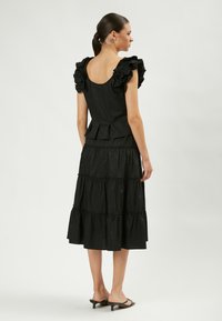 Vestido negro con un corsé ajustado, mangas con volantes y falda de capas. Hecho de un tejido ligero, tiene una cintura ceñida y un dobladillo acampanado.