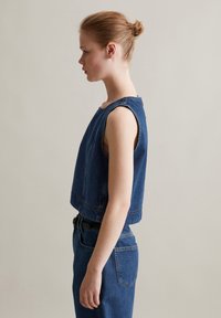 Jeansowy top w kolorze ciemnoniebieskim, bez rękawów, z okrągłym dekoltem i widocznym szwem. Połączony z spodniami o wysokim stanie, również w kolorze ciemnoniebieskim.