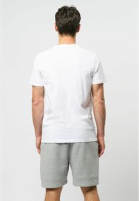 Balta 100% medvilnės marškinėliai su reguliariu pasiuvimu, trumpomis rankovėmis ir vientisa dizainu, derinami su pilkais megztiniais šortais, turinčiais apkarpytą galą.
