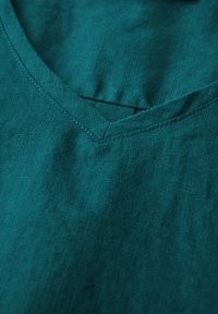 Tummansininen pellavakangas, jossa on V-kaula-aukko, joka esittelee hienovaraista tekstuuria ja siistiä ompelua kaula-aukon ympärillä.