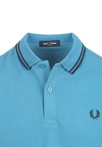 Polo shirt azzurro chiaro realizzato in cotone, caratterizzato da una superficie testurizzata, una chiusura con tre bottoni e un colletto a righe blu navy e bianche con logo ricamato.