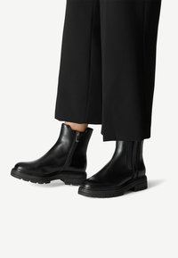 Bottines en cuir noir avec un design élégant, des fermetures éclair sur les côtés, des semelles épaisses et une texture lisse. Conviennent à diverses tenues.