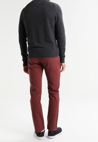 Tumma harmaa neulepaita yhdistettynä viininpunaisiin slim-fit-housuihin. Mallilla on päällä tummansiniset sneakersit. Housuissa on tavalliset taskut ja ompeluyksityiskohtia.