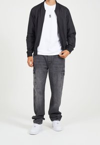 Svart bomberjacka, vit t-shirt, grå cargobyxor med fickor och vita sneakers. Slät tyg, avslappnad passform, minimalistisk design.