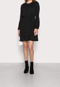 Czarna prążkowana sukienka z długimi rękawami, dopasowaną górą i ściąganym w pasie. Połączona z czarnymi botkami do kostki i małą białą torebką.