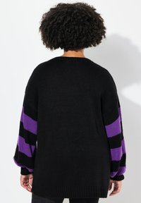Maglione nero lavorato a maglia con maniche a righe viola e nere, vestibilità rilassata e polsini e orlo a coste, dal tessuto morbido.