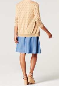Cardigan beige in maglia con motivo a diamante testurizzato, abbinato a una gona di jeans azzurra chiara. Sandali con zeppa e tacco in sughero completano il look.