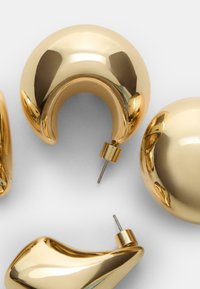 Boucles d'oreilles en or en forme de créole avec une surface lisse et réfléchissante, présentant des formes variées, y compris des designs arrondis et courbés, dotées de quincaillerie métallique.