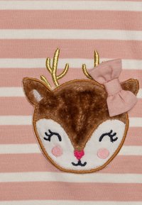 Usměvavá tvář jelena se zavřenýma očima, růžovými tvářičkami, růžovou mašlí na jednom uchu a zlatými parohy na růžovo-bílém pruhovaném pozadí.