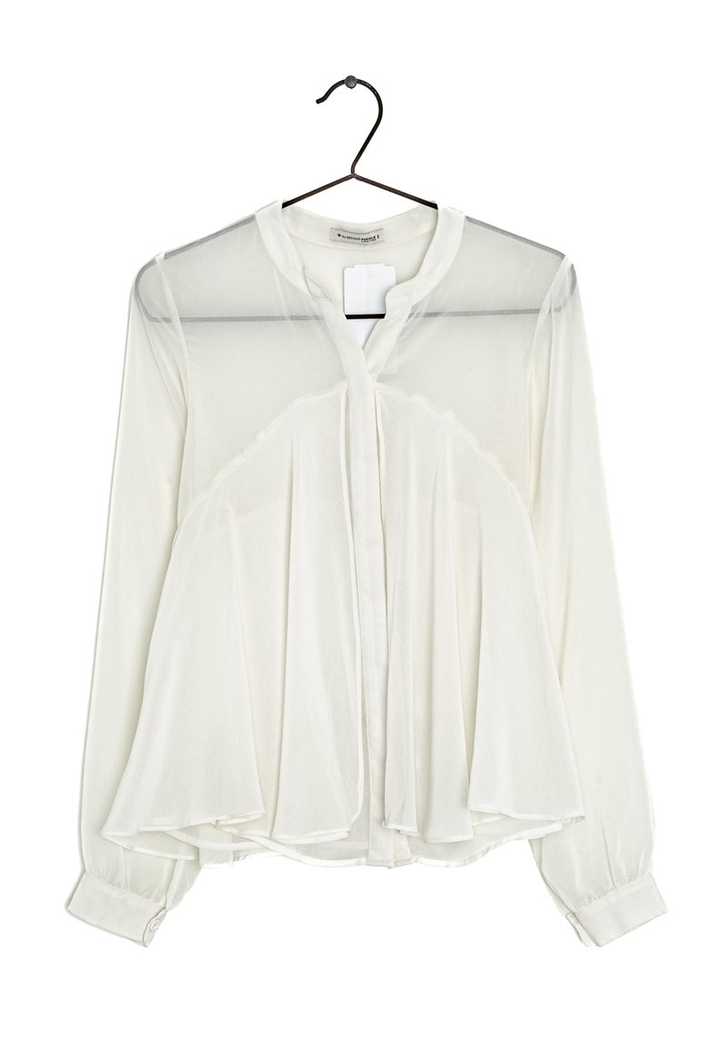 Vit blus med långa ärmar, genomskinlig frontpanel, knappstängning och rundad krage. Lättviktsmaterial med en flödande, lager-på-lager design.