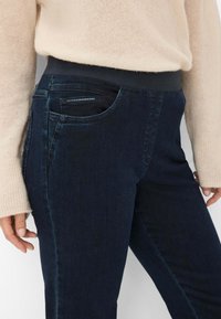 Donkerblauwe denim jeans met een rekbare tailleband, zijzakdetails en een slim fit ontwerp. De stof heeft een gladde en stevige textuur.