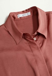 Camicetta rosa antico a maniche corte con una texture satinata liscia, caratterizzata da un colletto classico e una chiusura con un solo bottone al collo.