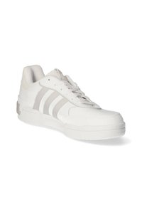 Zapato deportivo blanco de cuero liso con acentos grises, que presenta tres rayas en el costado, puntera redonda y suela de goma texturizada.