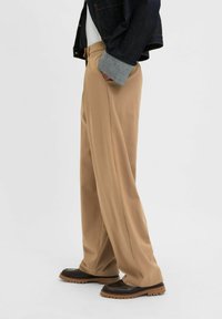 Beige broeken gemaakt van gladde stof, met een relaxte pasvorm en een rechte broekspijpen ontwerp. Gecombineerd met donker gekleurde schoenen en een spijkerjack.
