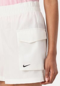 Nike-shorts i hvitt, med elastisk midjebånd og en frontlomme med klaff, samt en liten svart logo nær sømmen. Glatt, lett stoff.
