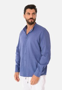 Camicia button-up blu con una texture morbida, dotata di colletto alla mandarino e maniche lunghe, rifinita con polsini arrotondati e sottili dettagli di cucitura.