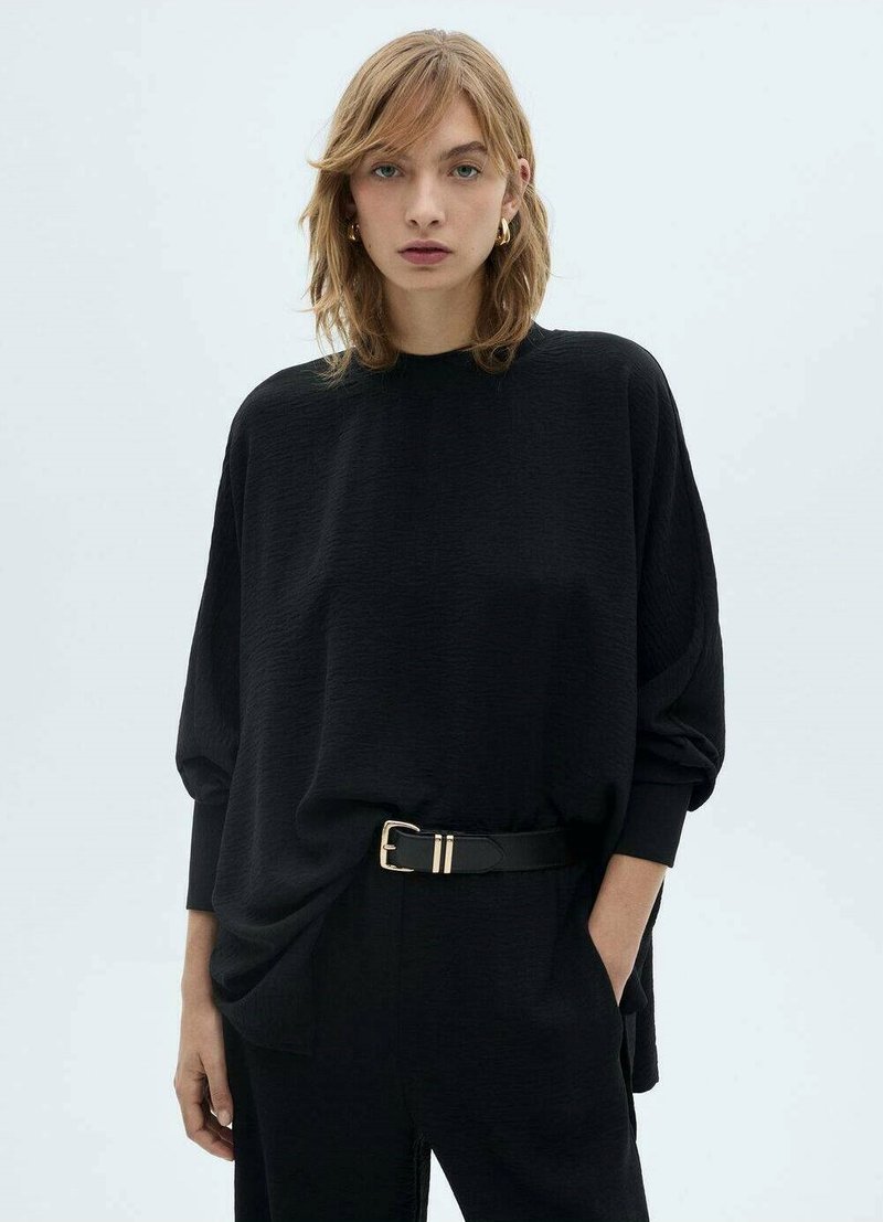 Maglietta nera oversize con scollo rotondo e maniche lunghe, caratterizzata da un tessuto testurizzato e una cintura nera con fibbia dorata in vita.
