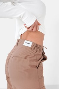 Lichtbruine cargobroek met een elastische tailleband, zijzakken en een label aan de achterkant, gecombineerd met een witte geribbelde langemouwen top.